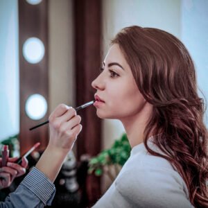Make up artist applying gloss on woman lips in modern beauty salon interior